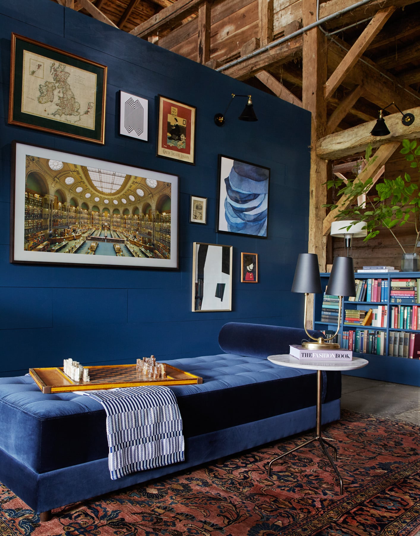 Blue velvet chaise lounge in front of blue wall with various framed maps, paintings and and photos hanging